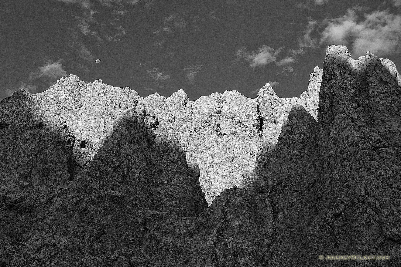 The first light of sunrise illuminates the erie rock formations deep in Badlands National Park as a waning moon gentle descends behind. - South Dakota Picture