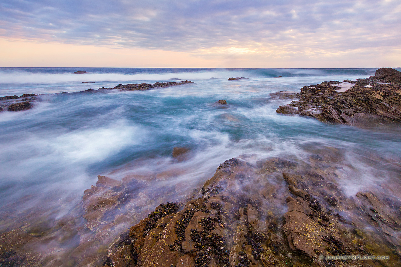 Waves wash around the rocks on the beach at Crystal Cove State Park, California while the sun sets in the distance. - State of California Picture