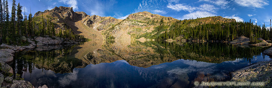 Deep in the backcountry of Rocky Mountain National Park, the mountains surrounding Lake Nokoni, sky and clouds reflect in the clear water. - Colorado Photography