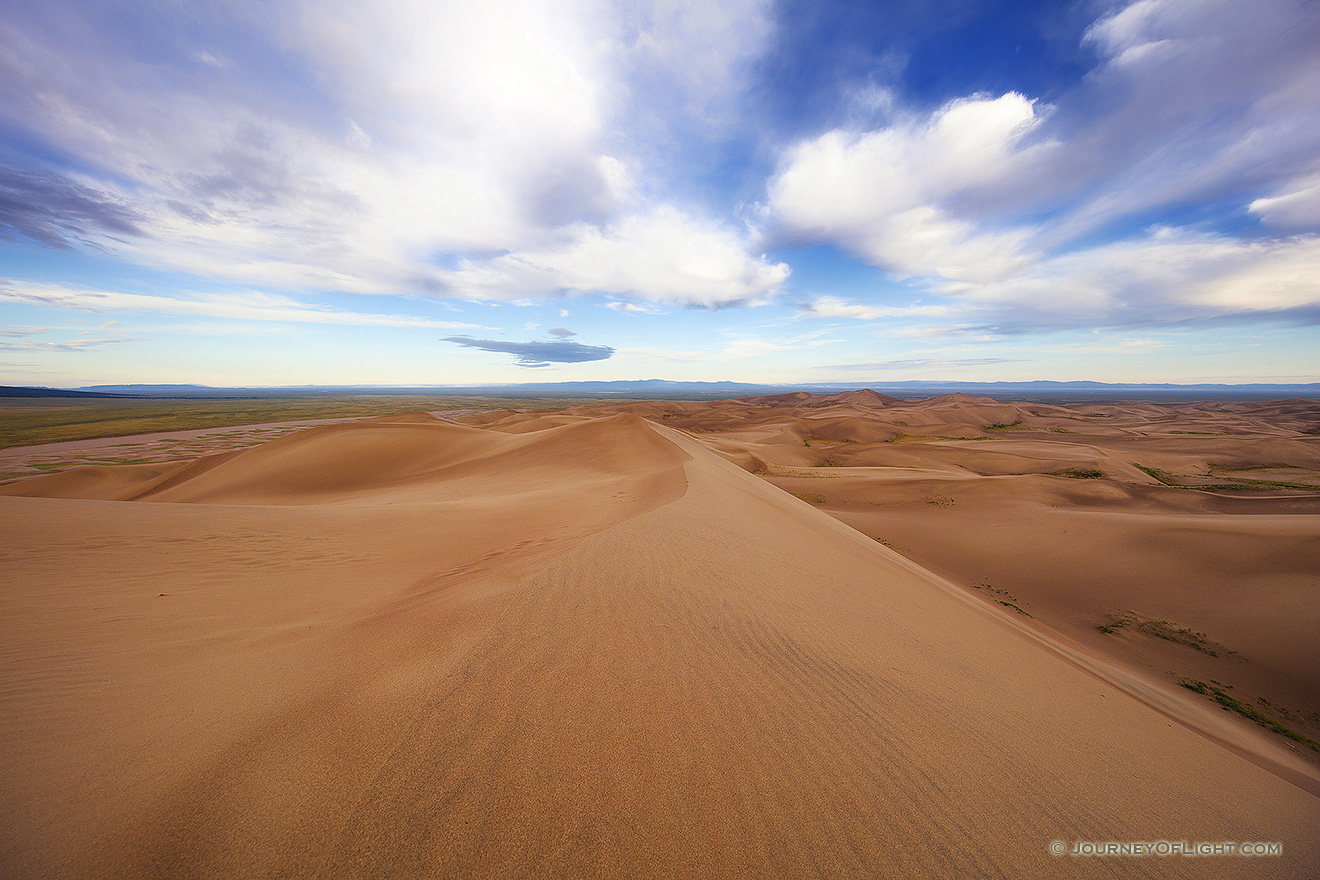 At Great Sand Dunes National Park and Preserve, dunes flow into the west as white clouds float high above. - Great Sand Dunes NP Picture