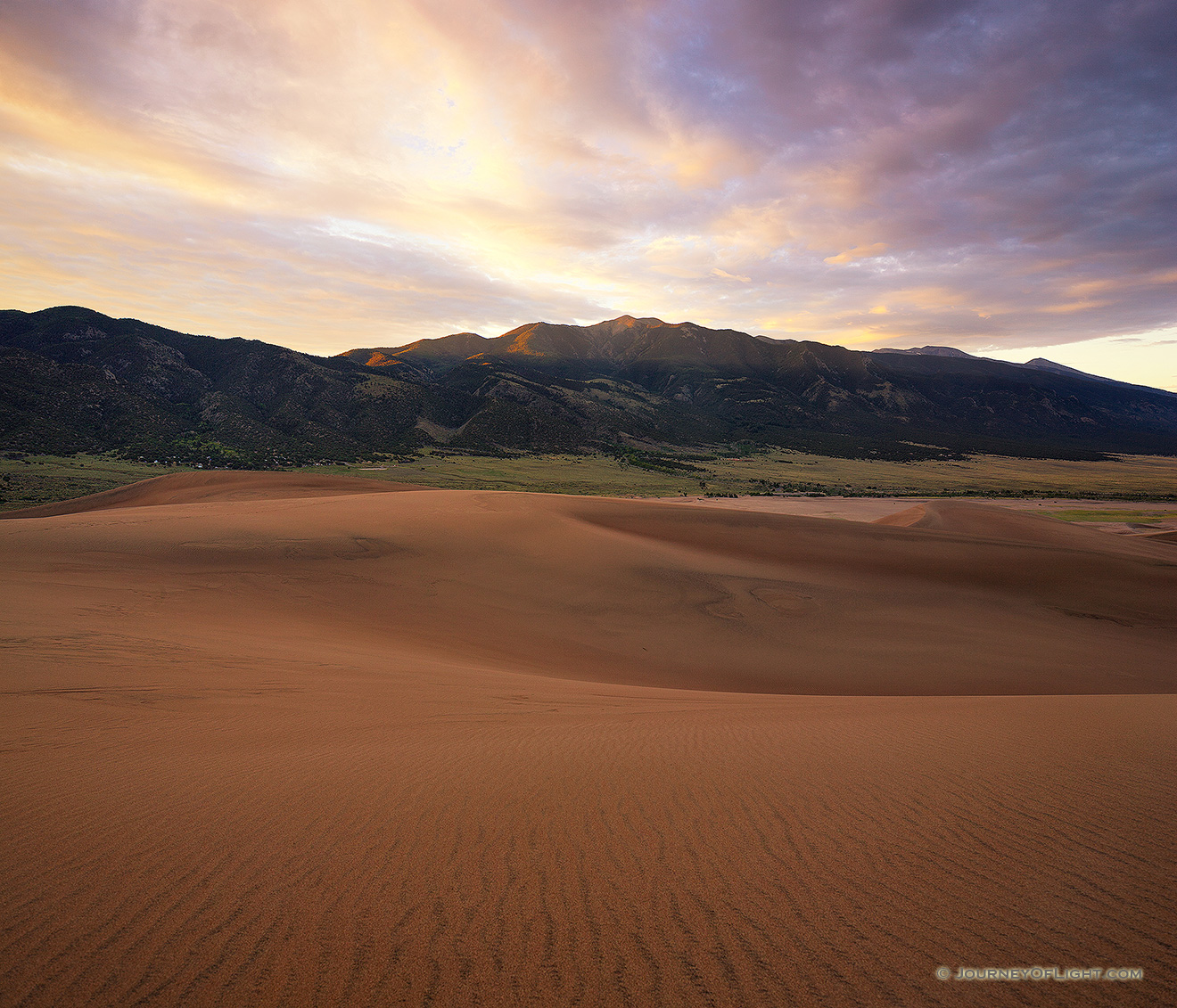 Sunlight streams through a pass in the Sangre de Cristo Mountains and illuminates the peak of Carbonate Mountain just southeast of the dunes at Great Sand Dune National Park. - Colorado Picture