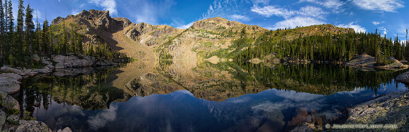 Deep in the backcountry of Rocky Mountain National Park, the mountains surrounding Lake Nokoni, sky and clouds reflect in the clear water. - Colorado Picture