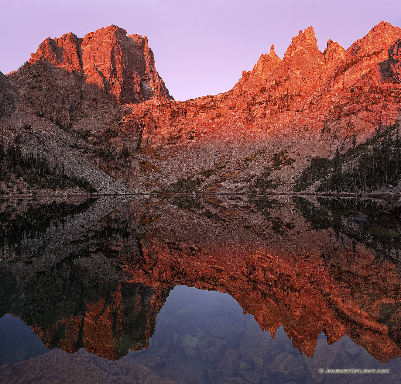 Unusually calm, Emerald Lake reflects a perfect and symmetrical image of the grand Hallet Peak and Flattop Mountain illuminated with alpenglow.  The only sounds on this quiet morning are the flow of a waterfall across the lake and the chirping of a nearby Steller's Jay. - Rocky Mountain NP Picture