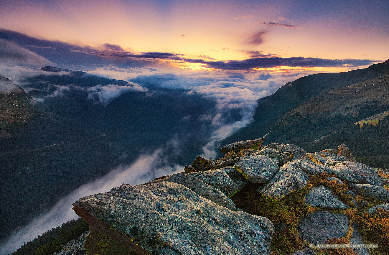 As clouds gather in the valley below, from the tundra of Rocky Mountain National Park, the sun sets behind the mountains of Colorado, the last rays burst forth with orange and yellow before dimming altogether. - Rocky Mountain NP Picture