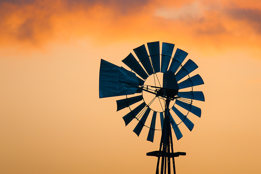 The orange glow of the sunset illuminates the last bits of clouds above an old windmill in western Iowa. - Iowa Photography