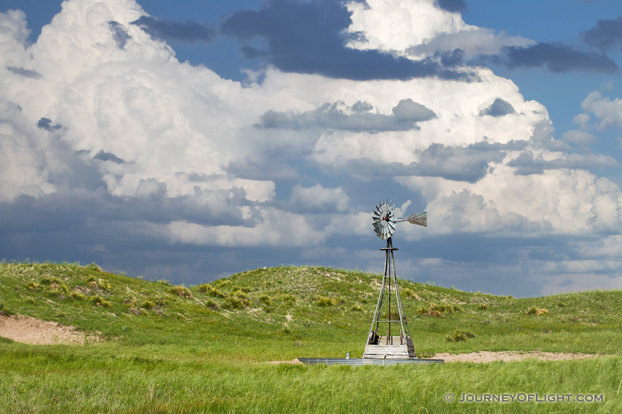 The sun shines on a windmill deep within the Sandhills of Nebraska as storm clouds roll in the distance. - Nebraska Photography