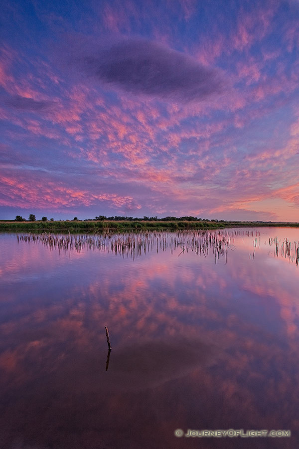 This photograph captures the light from the setting sun illuminating the underside of the higher clouds as a lone cloud floats through the scene. - Jack Sinn Photography