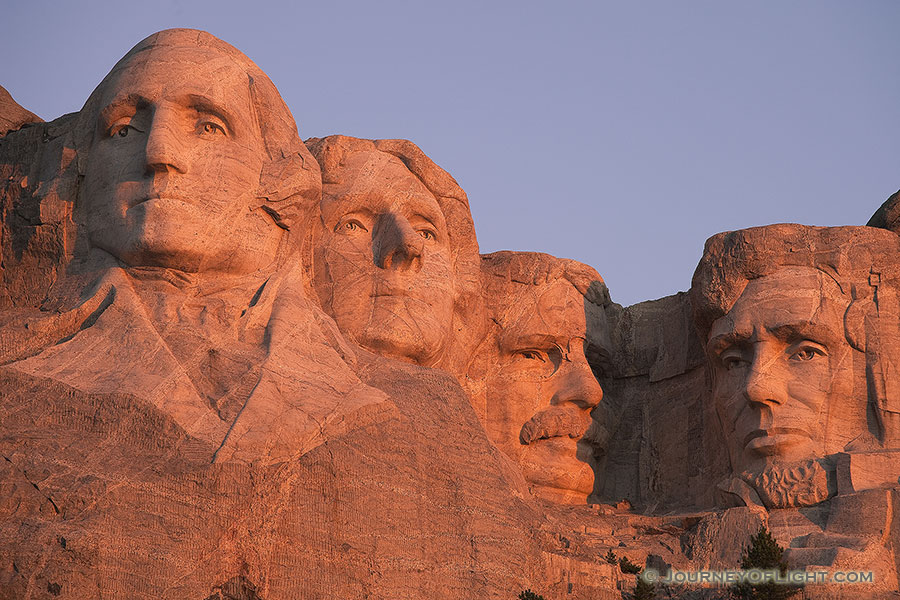 The warm sunrise light illuminates the faces with a reddish hue. - Mt. Rushmore NM Photography